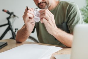 Telecommuter with creative block in home office crumpling sheet of paper